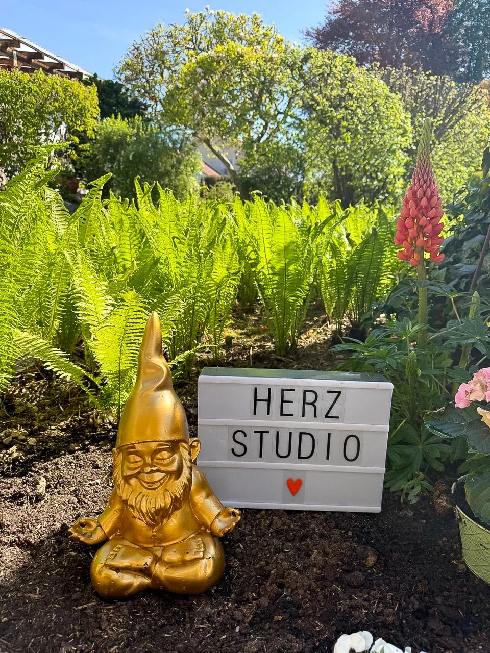 Herzstudio-Schild im Garten neben einem goldenen meditierenden Gartenzwerg